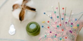 Poduszka z kolorowymi szpilkami, nicią i watą na stole w pracowni DIY