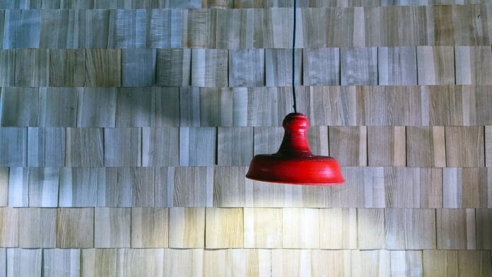 Czerwona lampa wisząca na tle drewnianej ściany z listewek Czerwona lampa wisząca na tle drewnianej ściany z listewek
